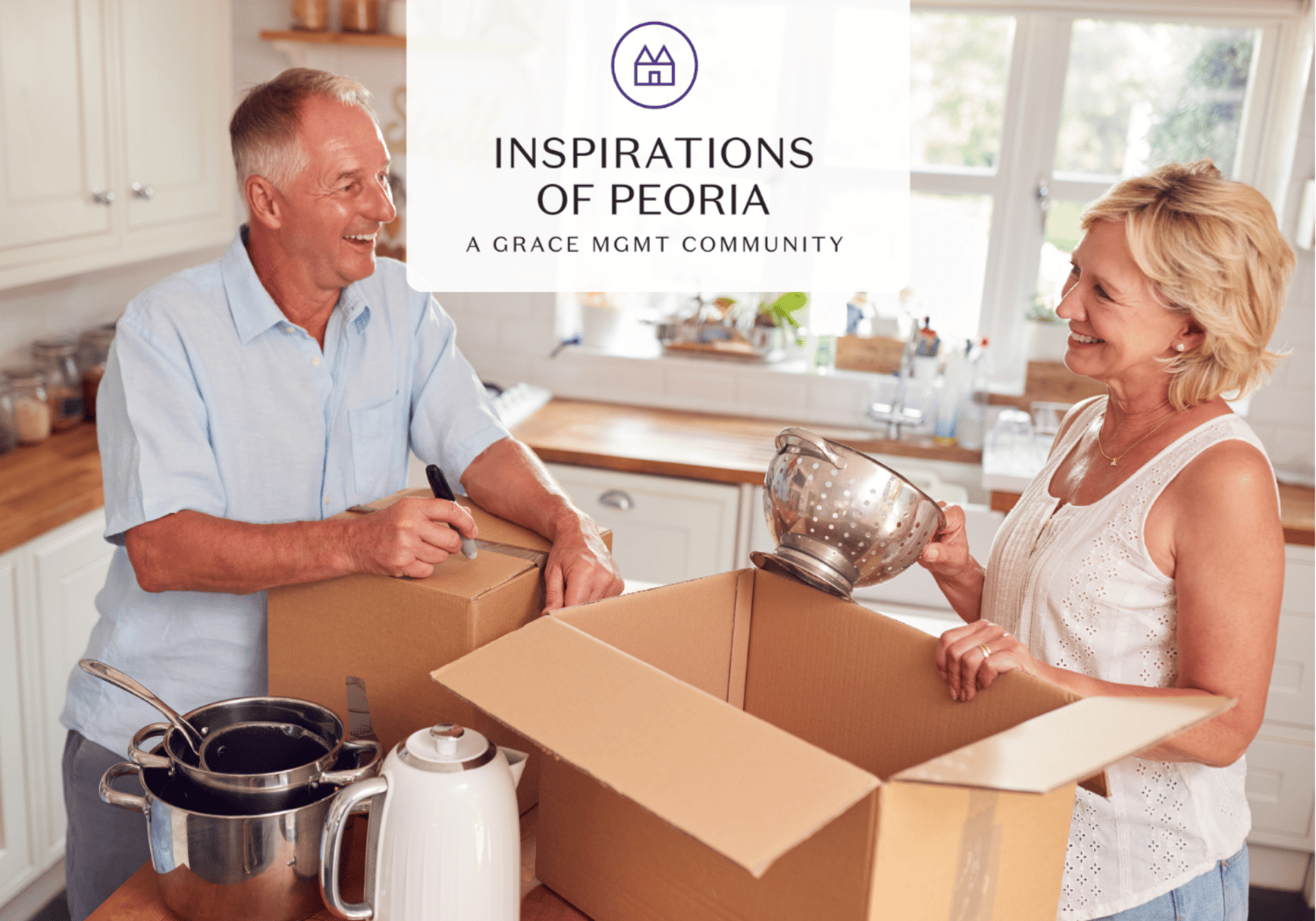 A smiling older couple packs a cardboard box in a bright kitchen, with pots and a kettle on the table nearby.