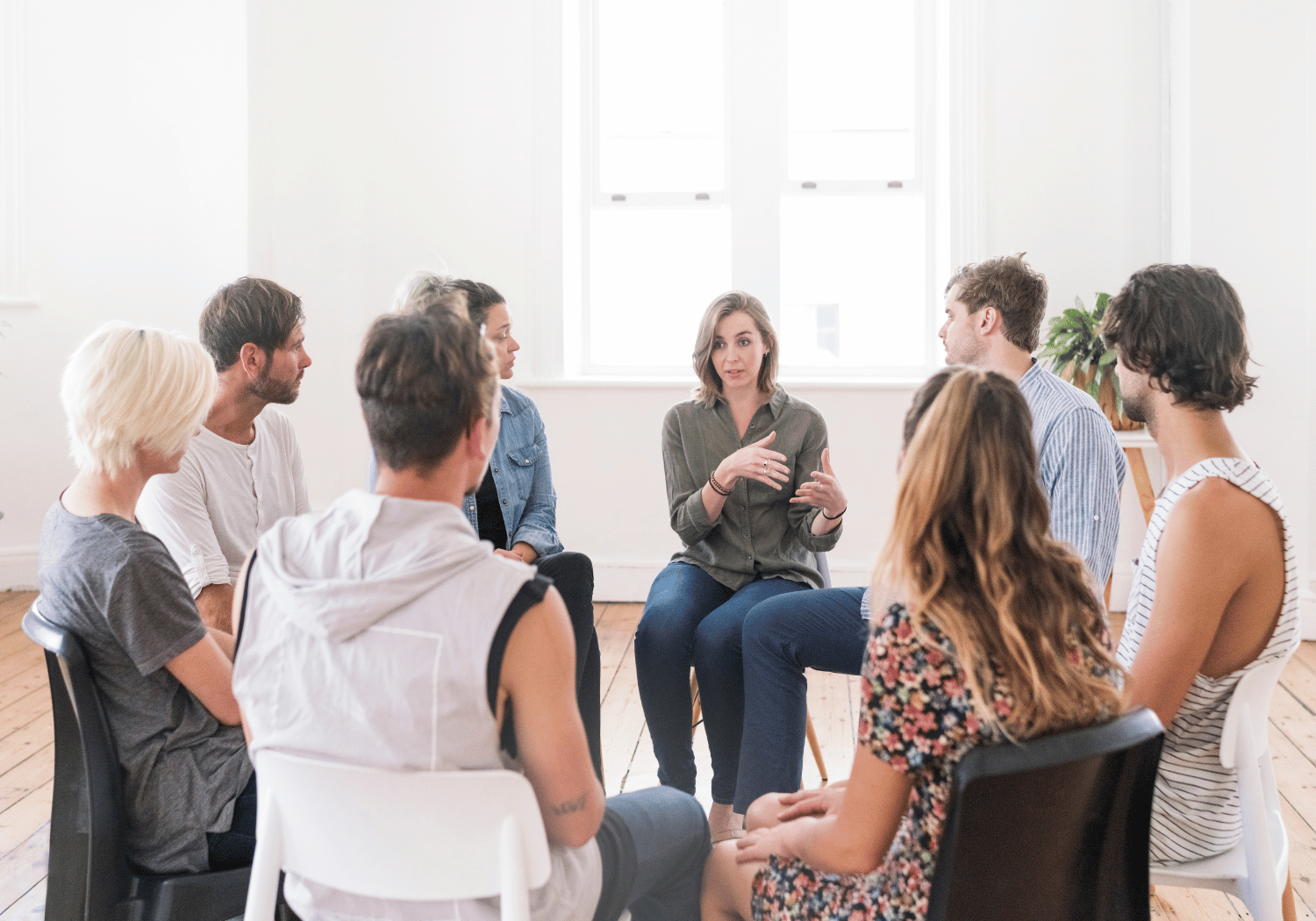 Woman leads a small group discussion in a bright room, seated in a circle listening and talking.